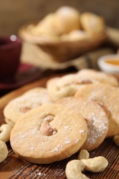 Photo of Tasty cashew cookies with powdered sugar on wooden board, closeup