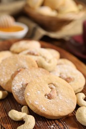 Photo of Tasty cashew cookies with powdered sugar on wooden board, closeup