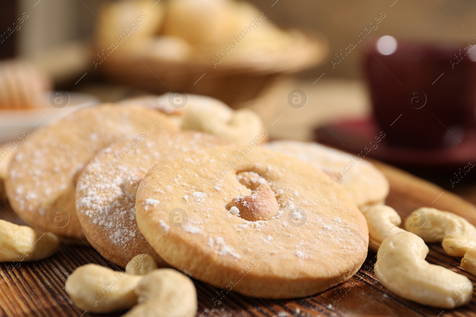 Photo of Tasty cashew cookies with powdered sugar on wooden board, closeup