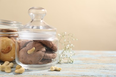 Photo of Different tasty cashew cookies in jars on light wooden table against beige background, closeup. Space for text