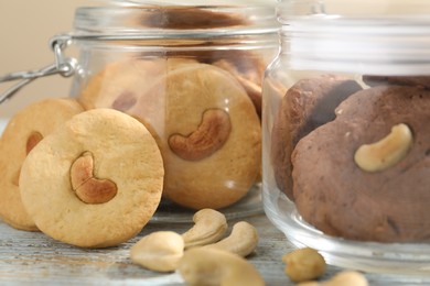 Photo of Different tasty cashew cookies in jars on light wooden table, closeup