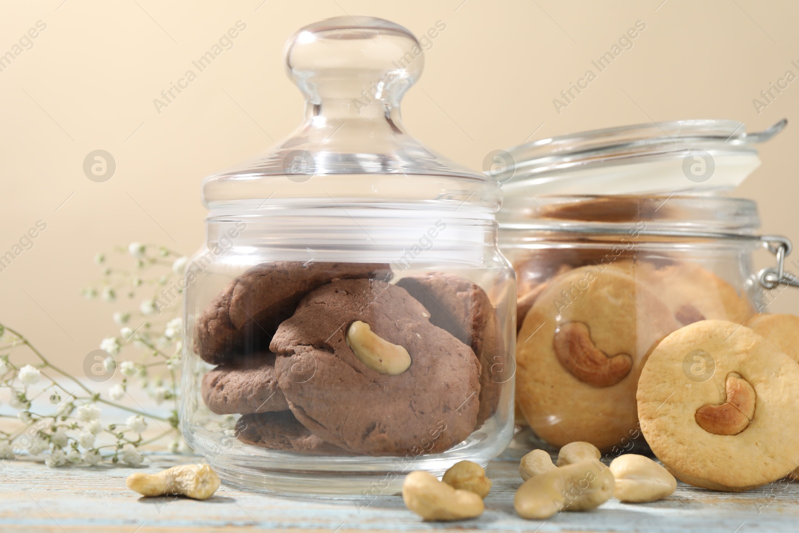 Photo of Different tasty cashew cookies in jars on light wooden table against beige background, closeup