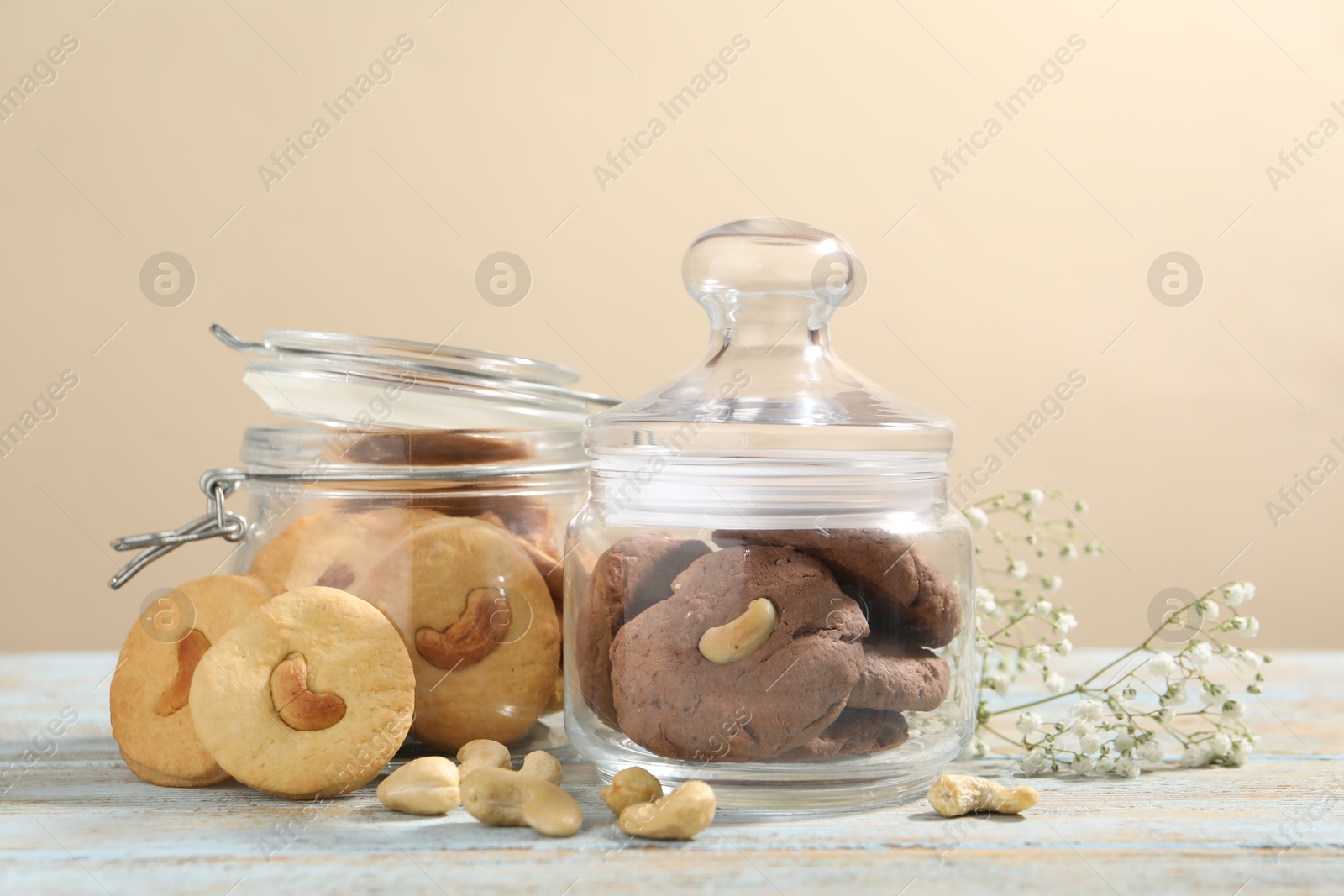 Photo of Different tasty cashew cookies in jars on light wooden table against beige background, closeup