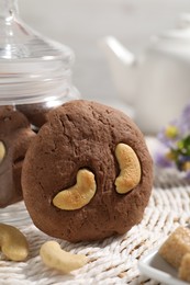 Photo of Tasty chocolate cookies with cashew on wicker mat, closeup