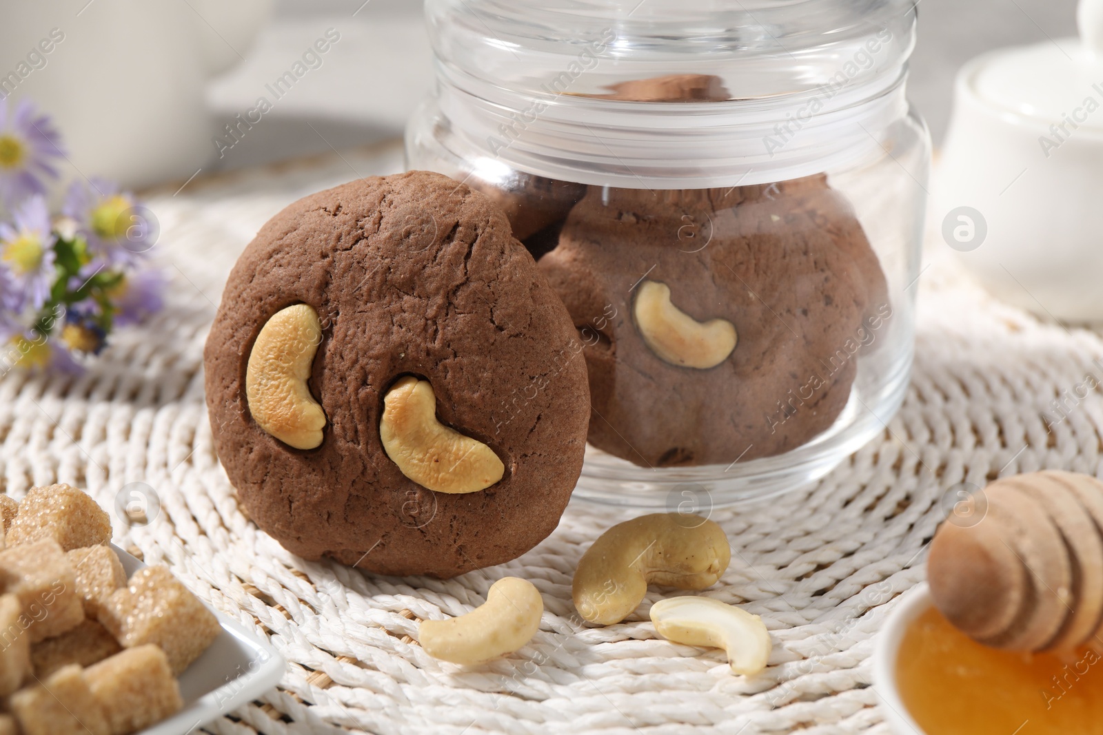 Photo of Tasty chocolate cookies with cashew on wicker mat, closeup