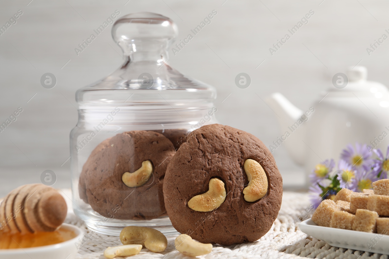 Photo of Tasty chocolate cookies with cashew, honey and sugar cubes on wicker mat, closeup