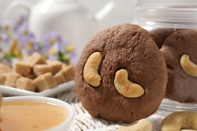 Photo of Tasty chocolate cookies with cashew on wicker mat, closeup