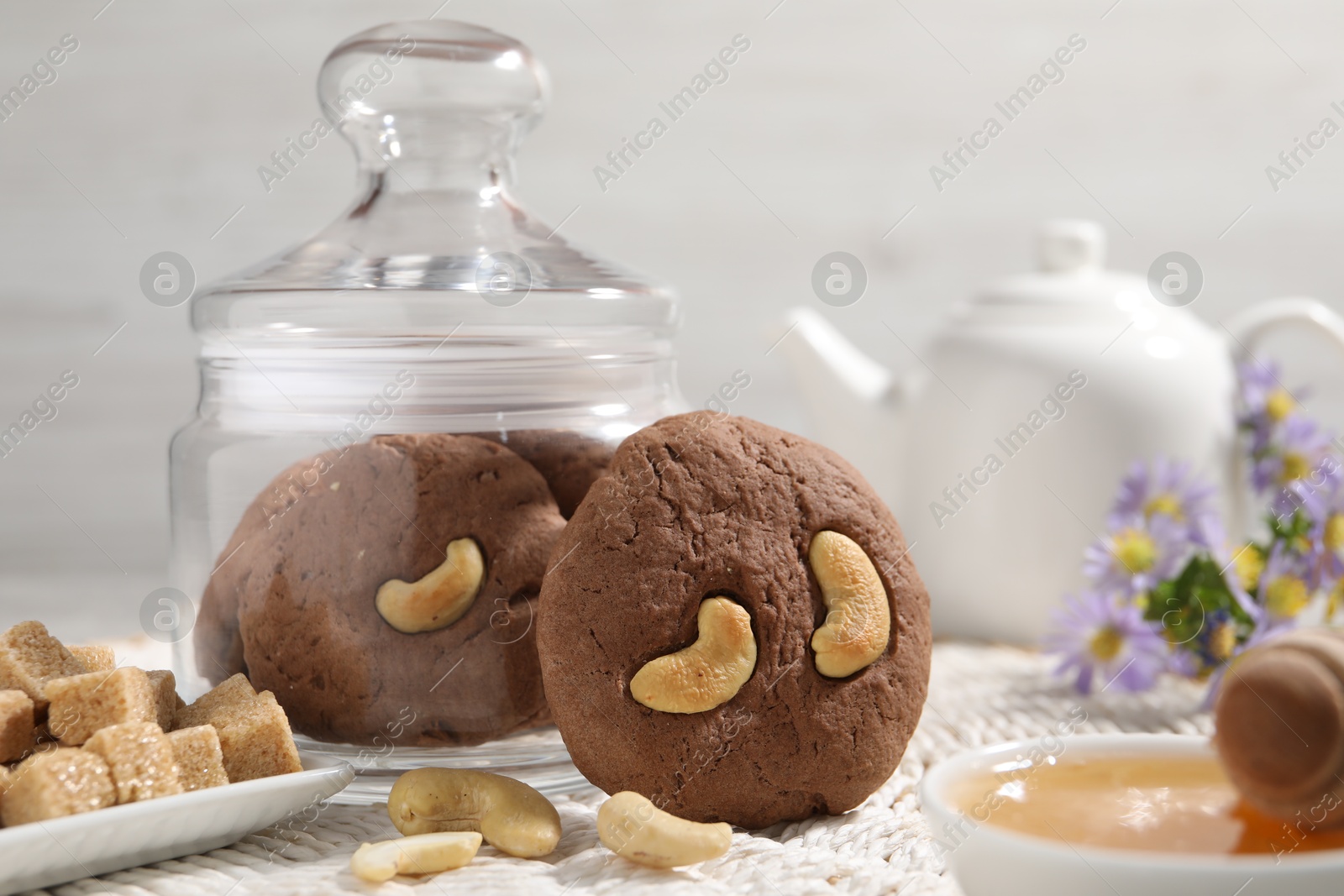 Photo of Tasty chocolate cookies with cashew, honey and sugar cubes on wicker mat, closeup