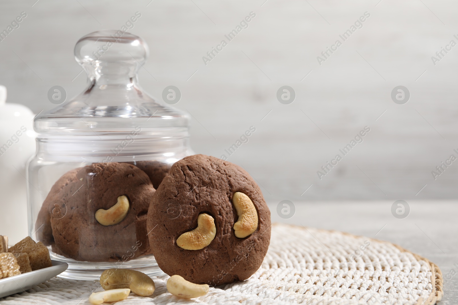 Photo of Tasty chocolate cookies with cashew on wicker mat, closeup. Space for text