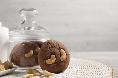 Photo of Tasty chocolate cookies with cashew on wicker mat, closeup. Space for text