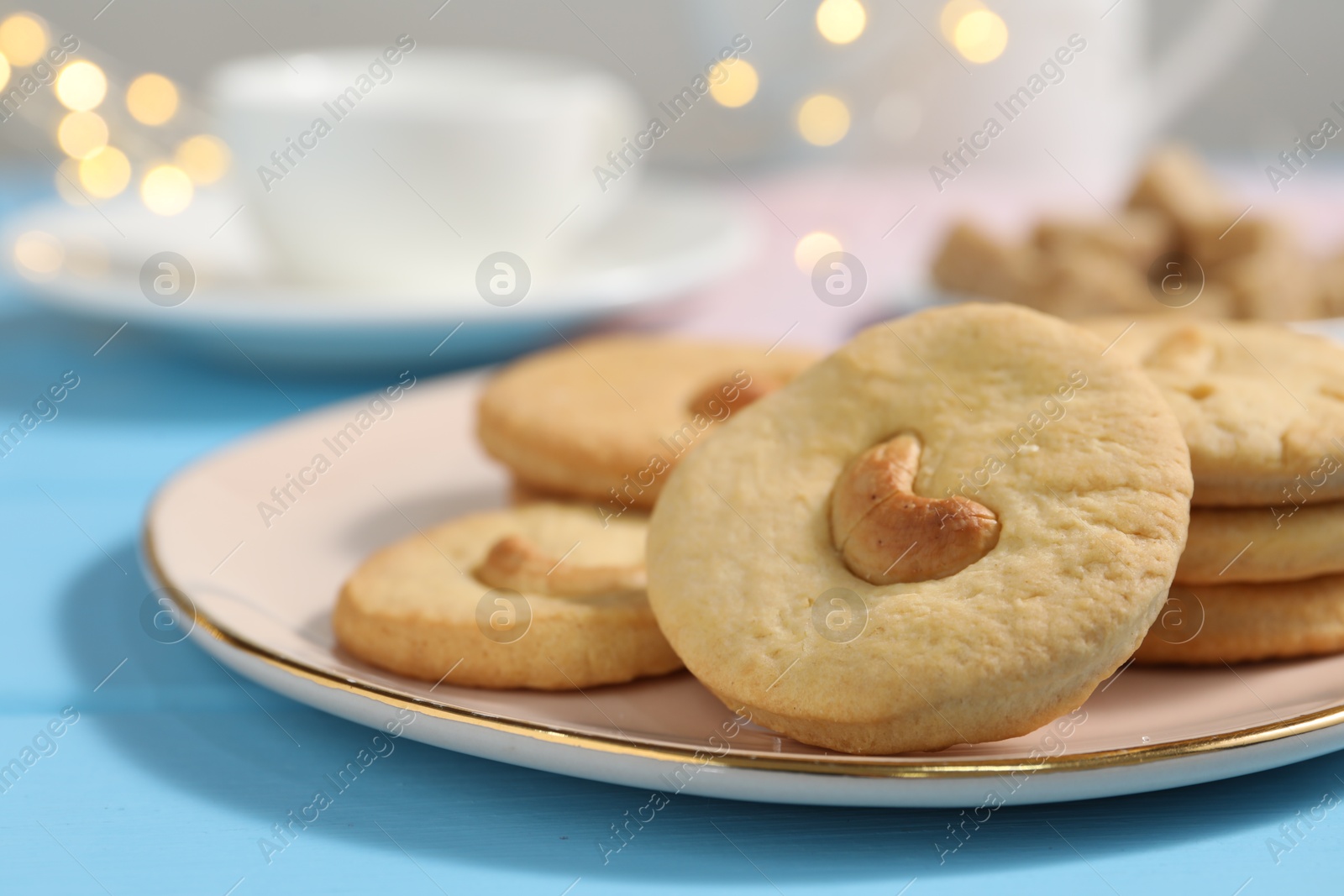 Photo of Plate with tasty cashew cookies on light blue wooden table, closeup