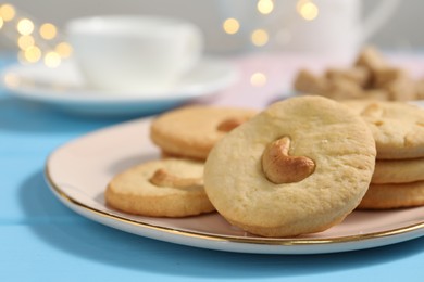 Photo of Plate with tasty cashew cookies on light blue wooden table, closeup