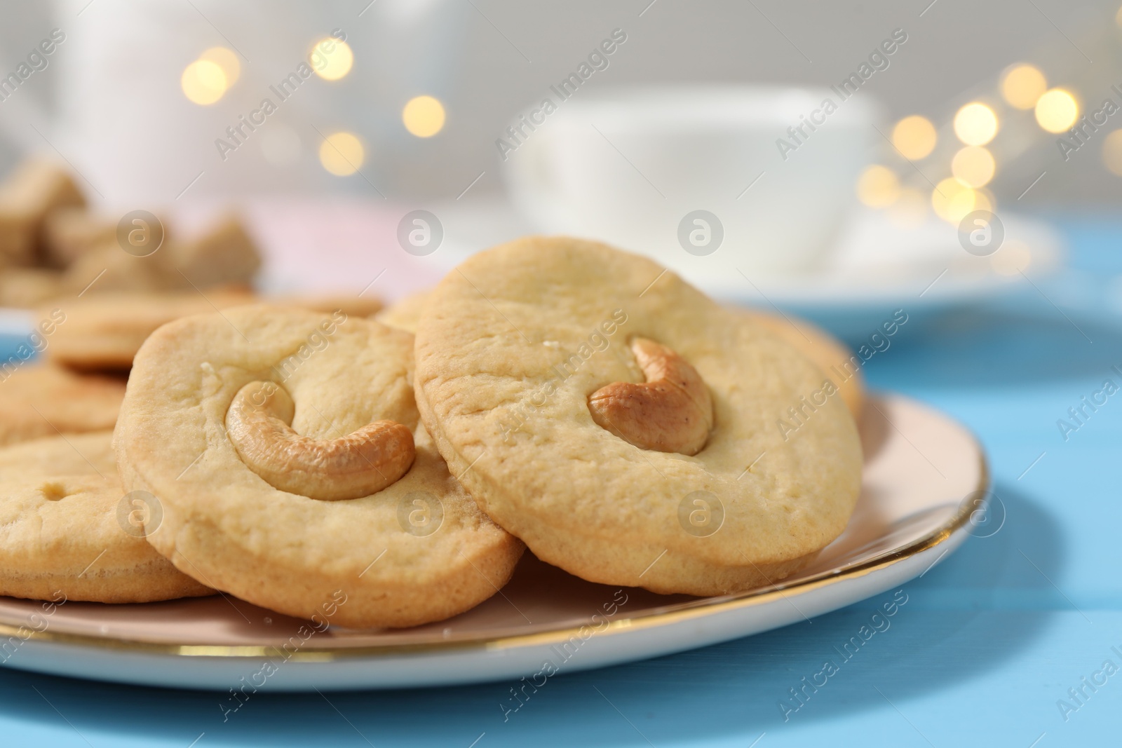 Photo of Plate with tasty cashew cookies on light blue wooden table, closeup