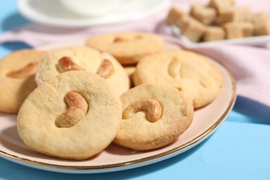 Photo of Plate with tasty cashew cookies on light blue wooden table, closeup