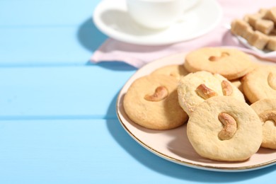 Photo of Plate with tasty cashew cookies on light blue wooden table, closeup. Space for text