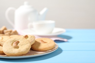 Photo of Plate with tasty cashew cookies on light blue wooden table, closeup. Space for text