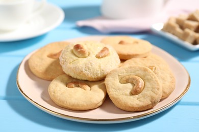 Photo of Plate with tasty cashew cookies on light blue wooden table, closeup