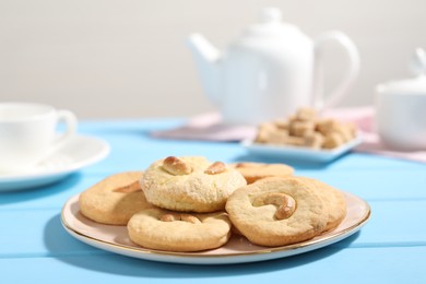 Photo of Plate with tasty cashew cookies on light blue wooden table, closeup