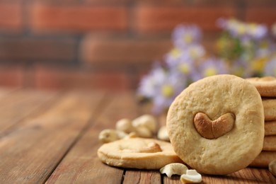 Photo of Tasty cashew cookies on wooden table against brick wall, closeup. Space for text