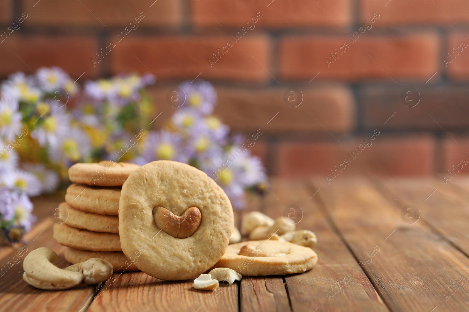 Photo of Tasty cashew cookies on wooden table against brick wall, closeup. Space for text