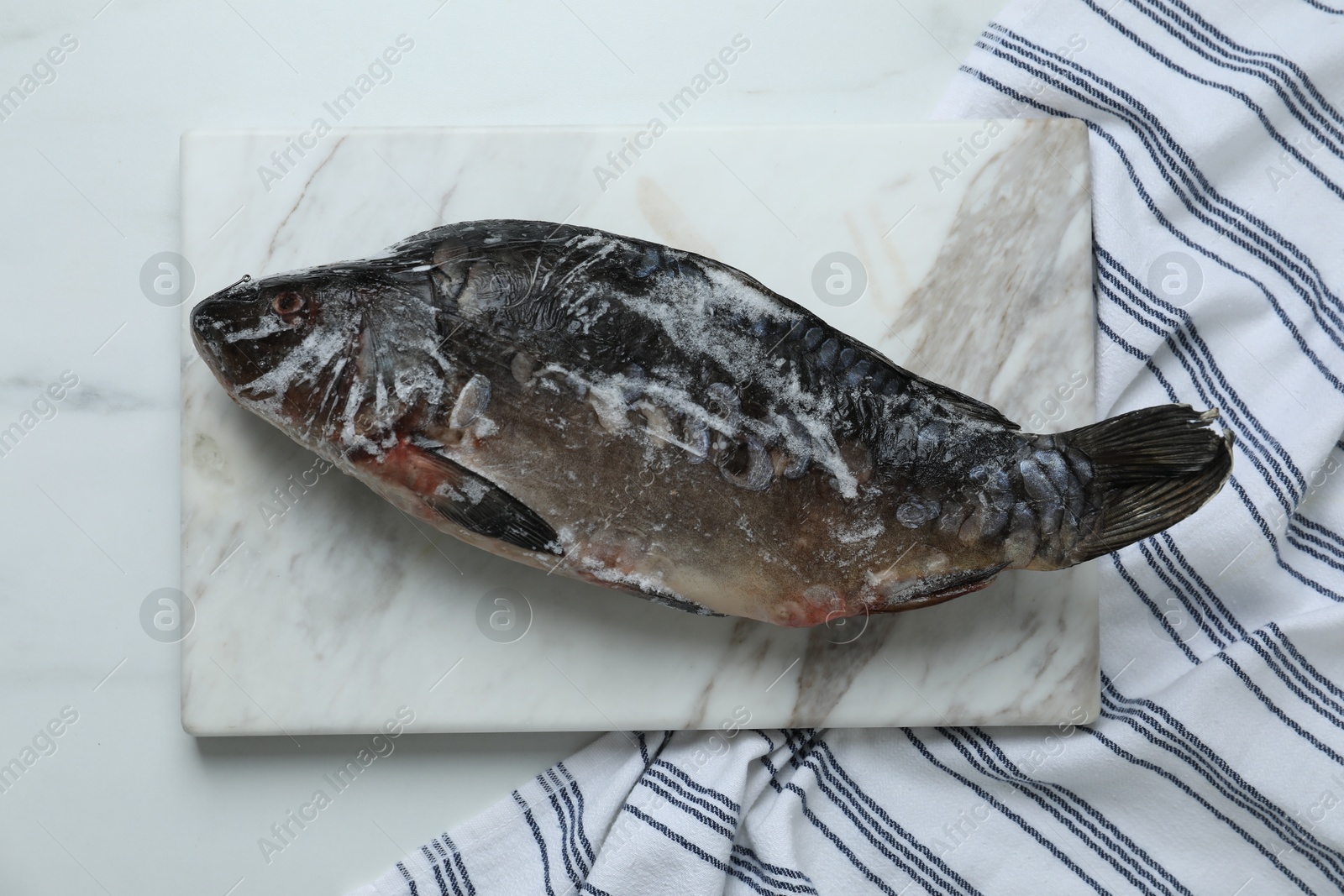 Photo of Frozen carp fish on white marble table, top view