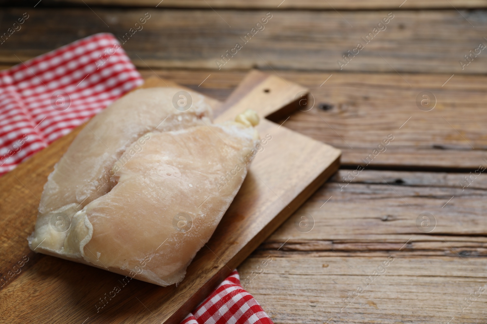 Photo of Frozen chicken breasts on wooden table, closeup. Space for text