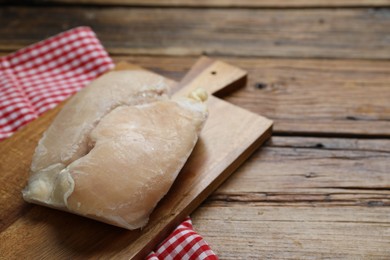 Photo of Frozen chicken breasts on wooden table, closeup. Space for text