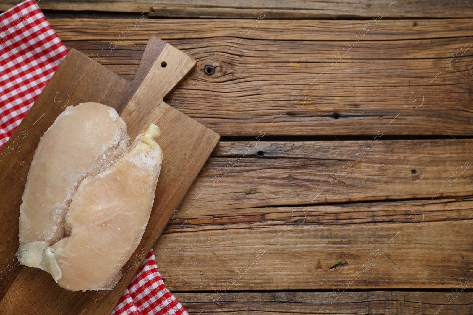 Photo of Frozen chicken breasts on wooden table, top view. Space for text