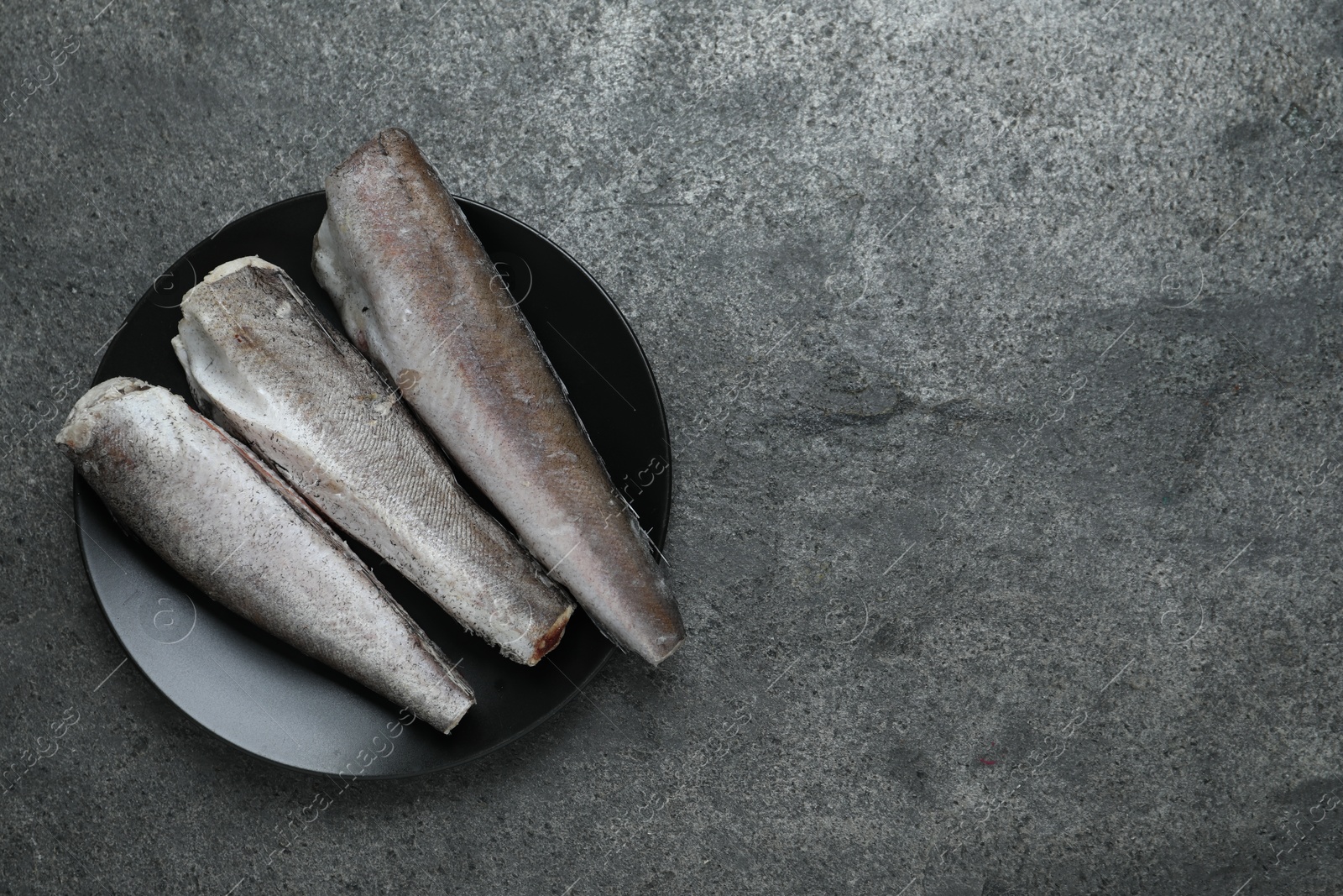 Photo of Frozen hake fishes on grey table, top view. Space for text