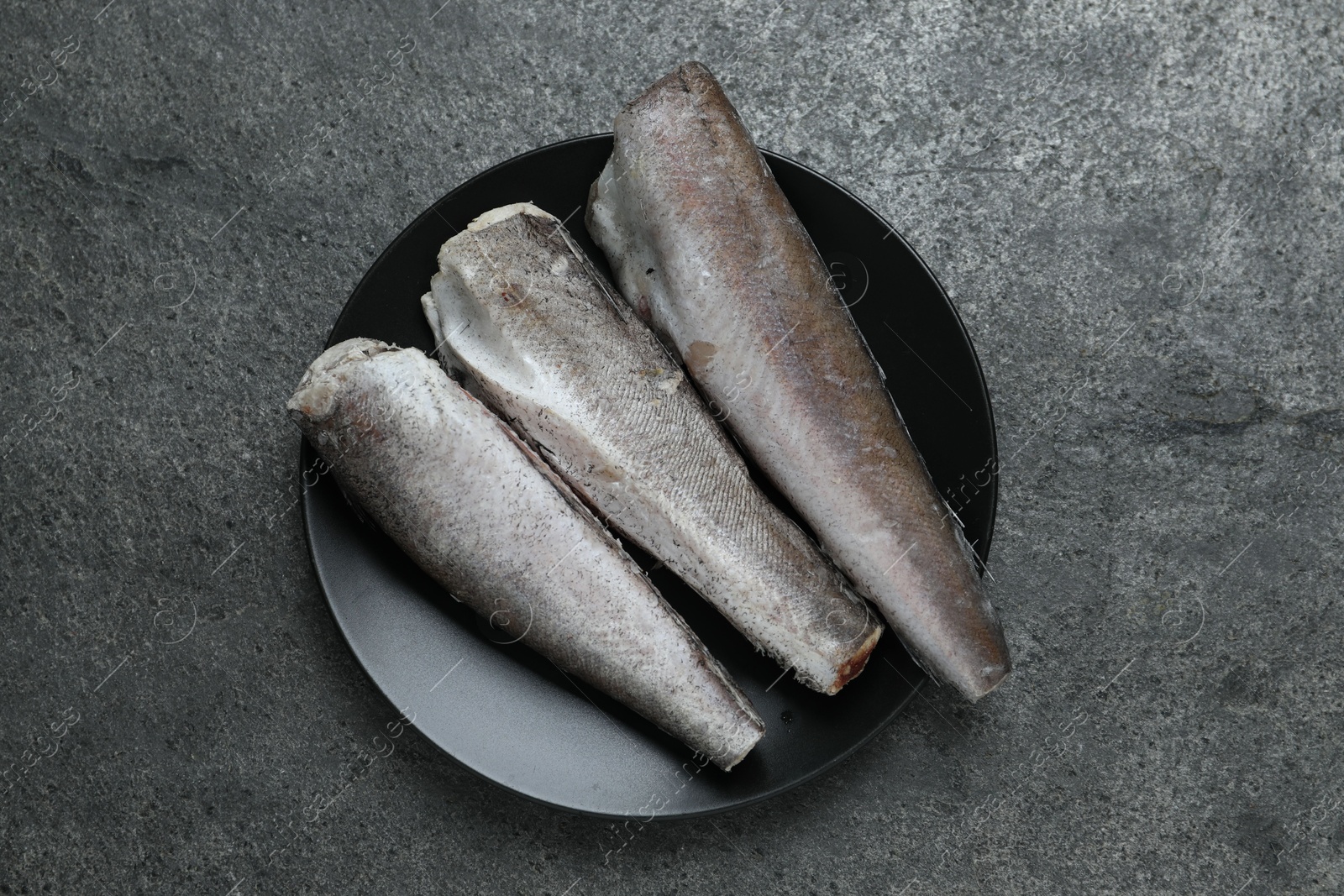 Photo of Frozen hake fishes on grey table, top view