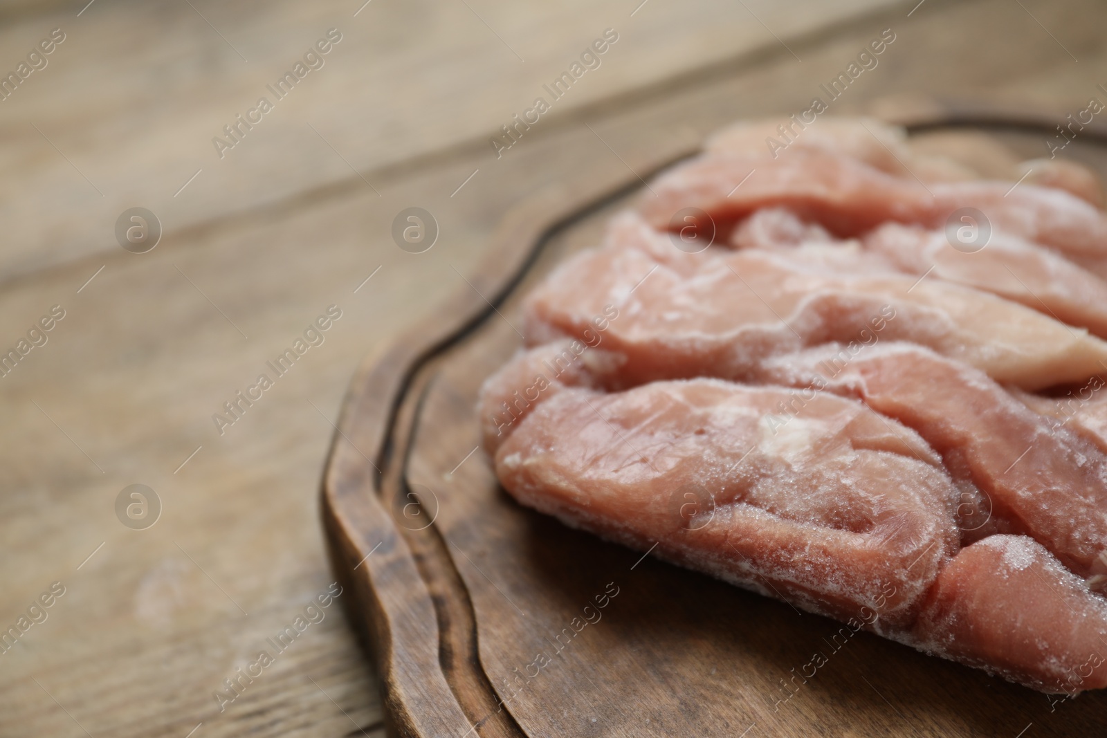 Photo of Frozen pieces of chicken fillet on wooden table, closeup. Space for text