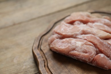 Photo of Frozen pieces of chicken fillet on wooden table, closeup. Space for text