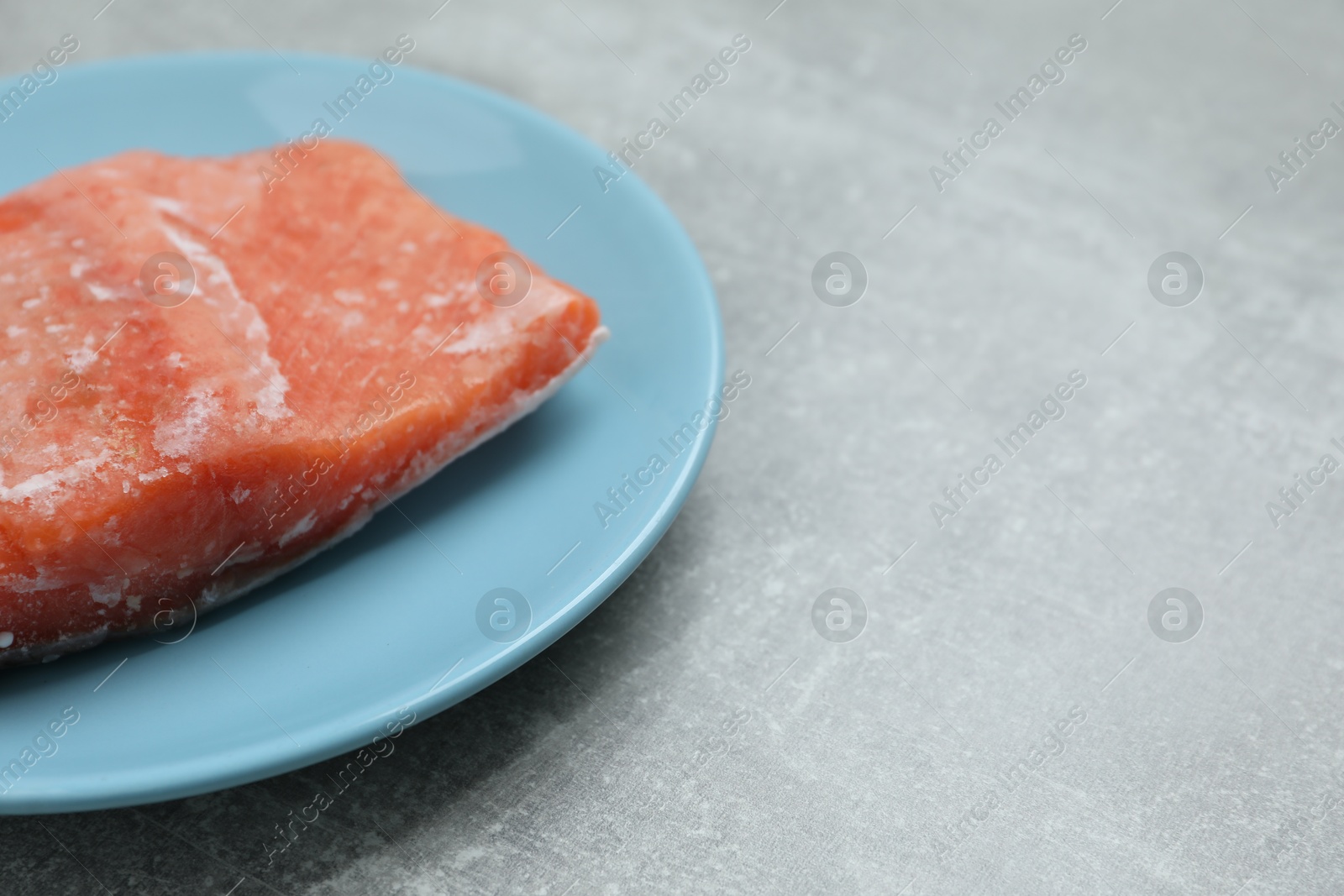 Photo of Frozen piece of salmon on grey table, closeup. Space for text