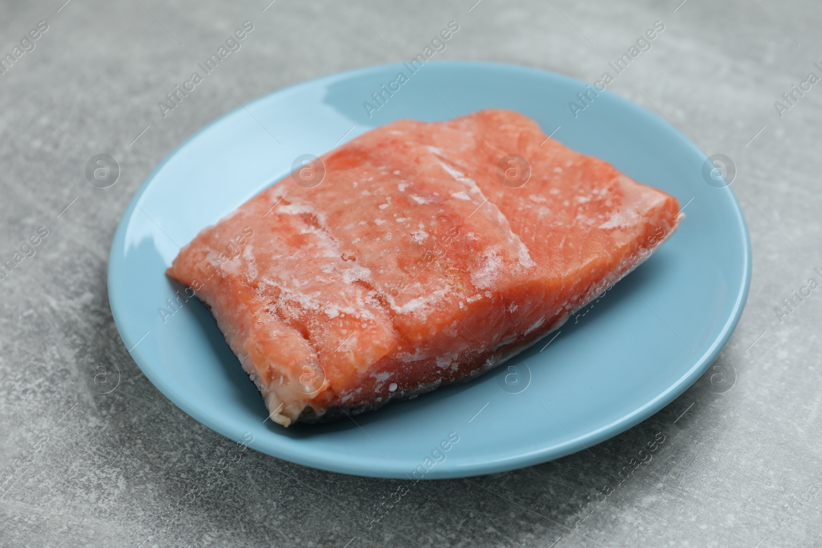 Photo of Frozen piece of salmon on grey table, closeup