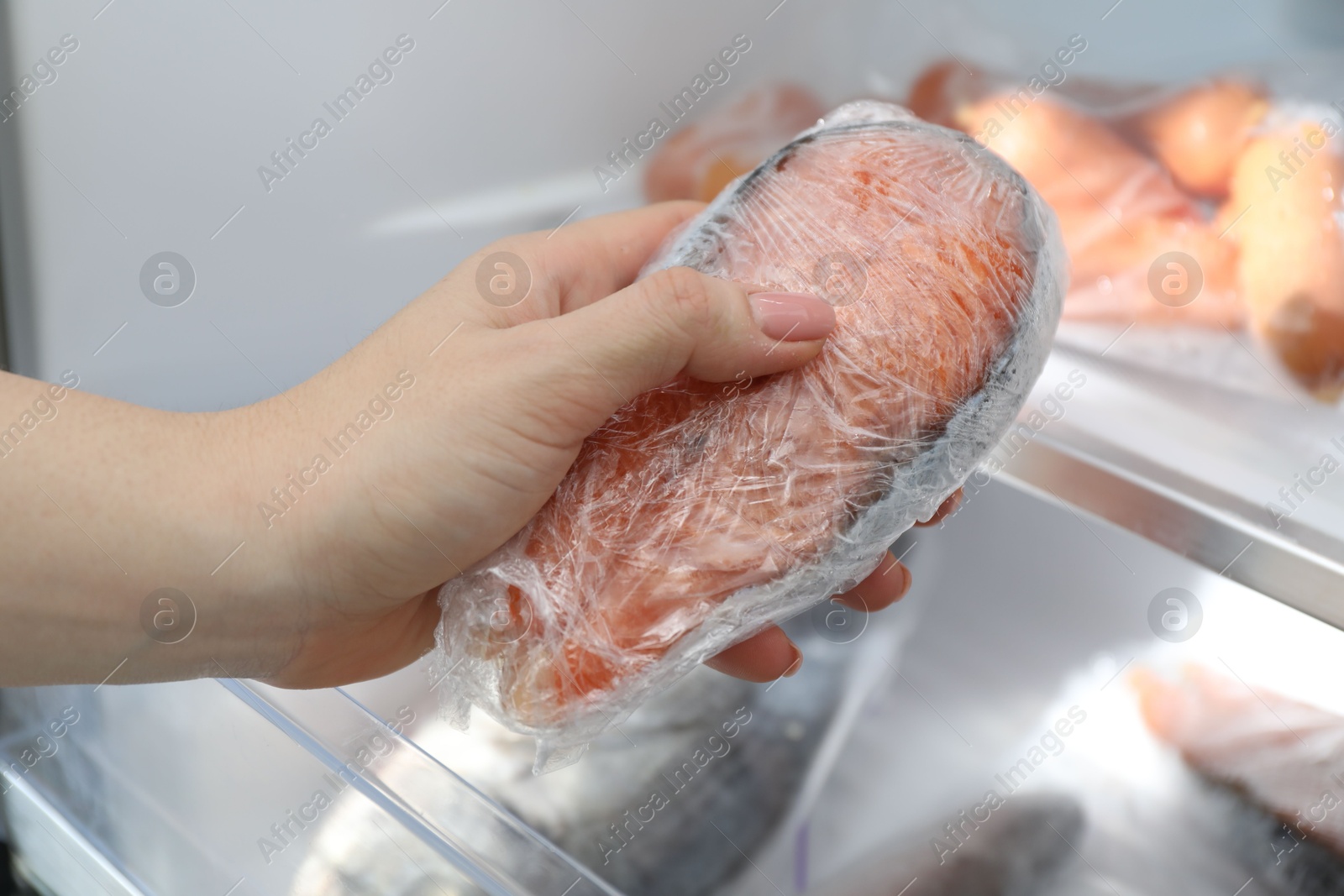 Photo of Woman taking frozen salmon steak out of fridge, closeup