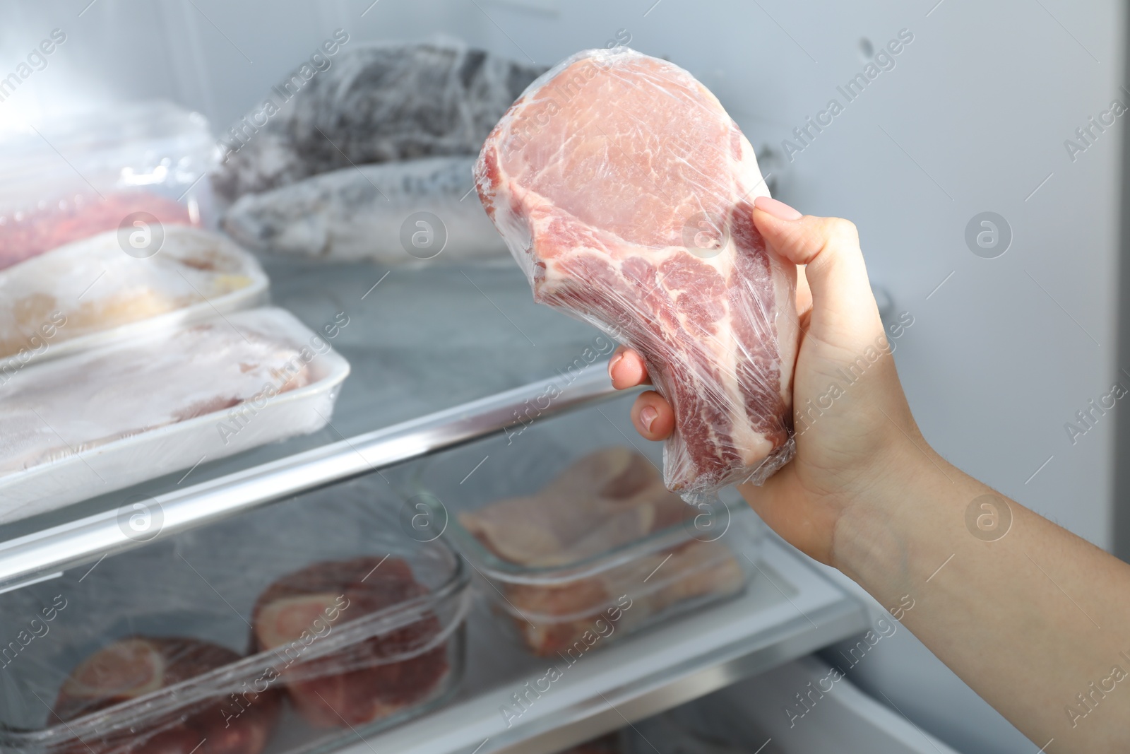 Photo of Woman taking frozen pork steak out of fridge, closeup