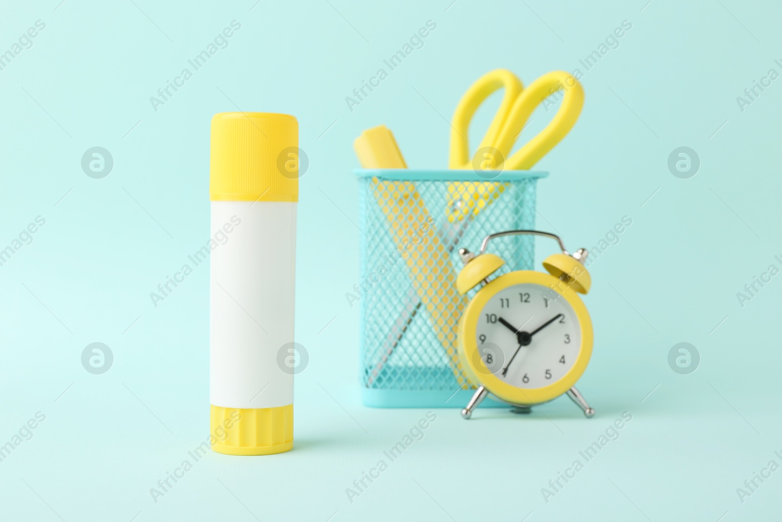 Photo of Glue stick, alarm clock, holder and scissors on turquoise background