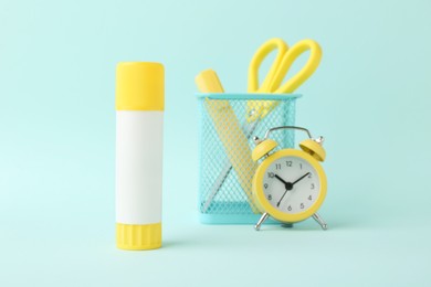 Photo of Glue stick, alarm clock, holder and scissors on turquoise background