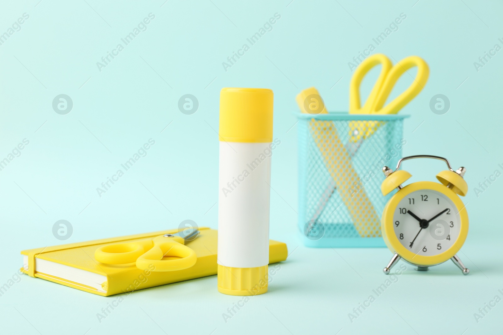 Photo of Glue stick, alarm clock, holder, scissors and notebook on turquoise background