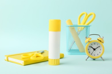 Photo of Glue stick, alarm clock, holder, scissors and notebook on turquoise background