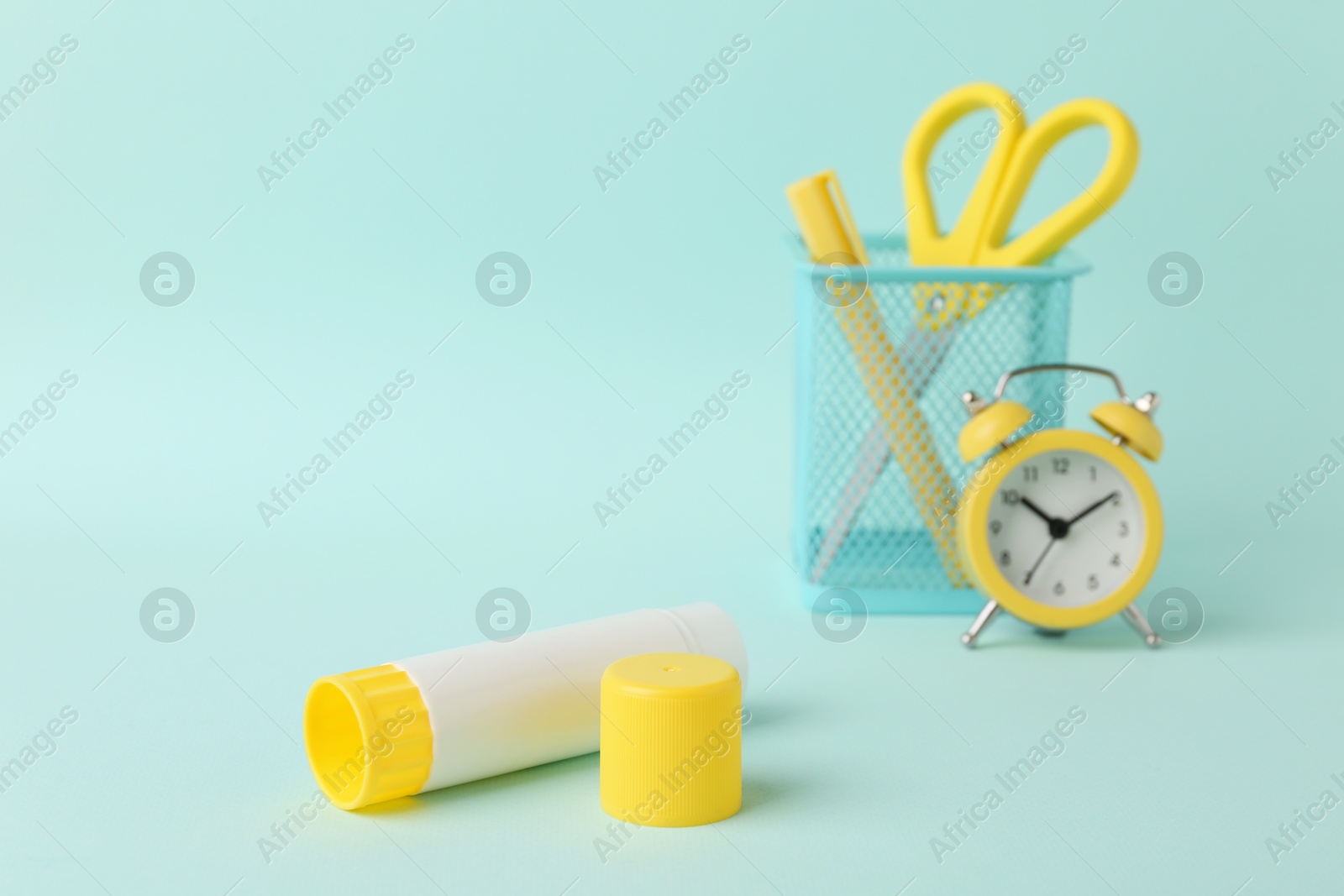 Photo of Glue stick, alarm clock, holder and scissors on turquoise background