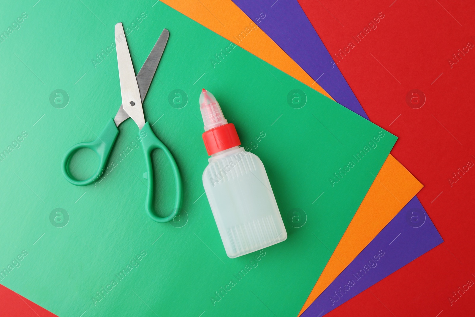 Photo of Bottle of glue, scissors and colorful paper on red background, flat lay