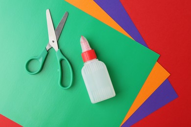 Bottle of glue, scissors and colorful paper on red background, flat lay