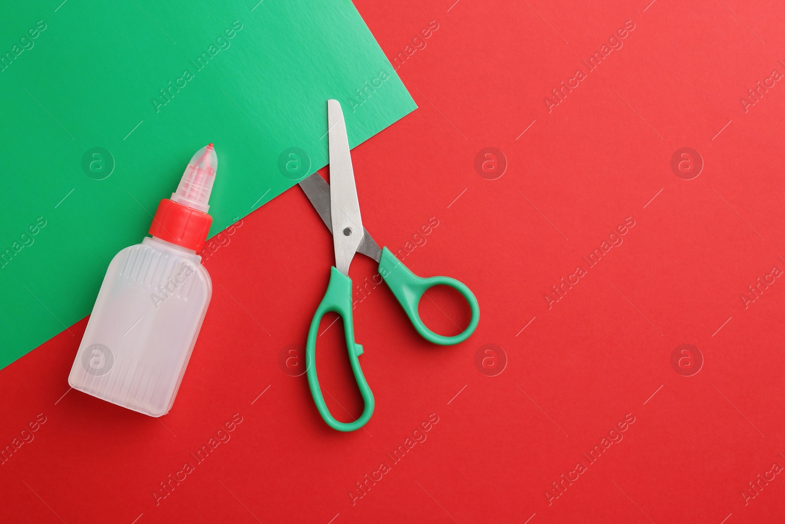 Photo of Bottle of glue, scissors and green paper on red background, flat lay. Space for text