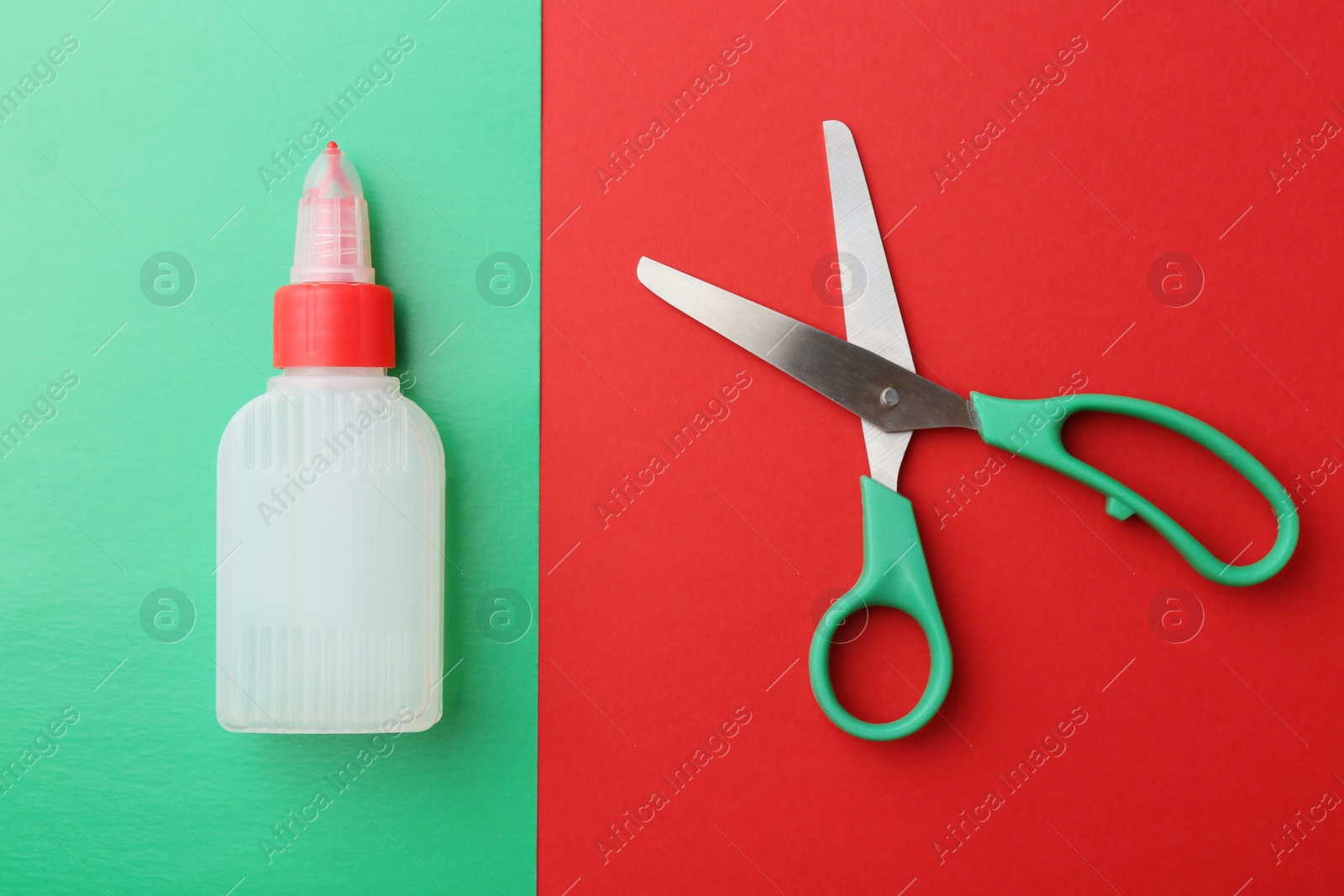 Photo of Bottle of glue, scissors and green paper on red background, flat lay