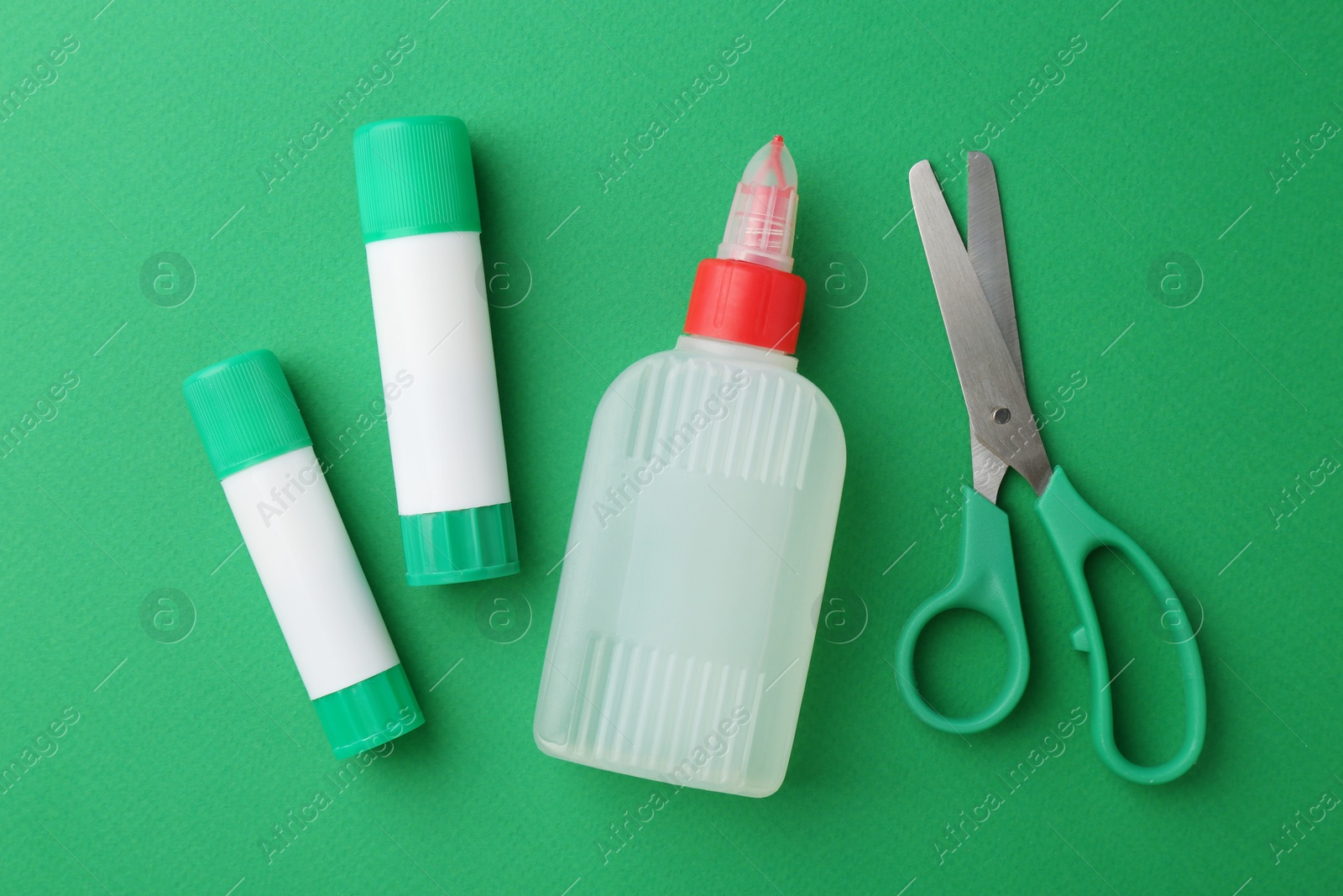 Photo of Glue and scissors on green background, flat lay