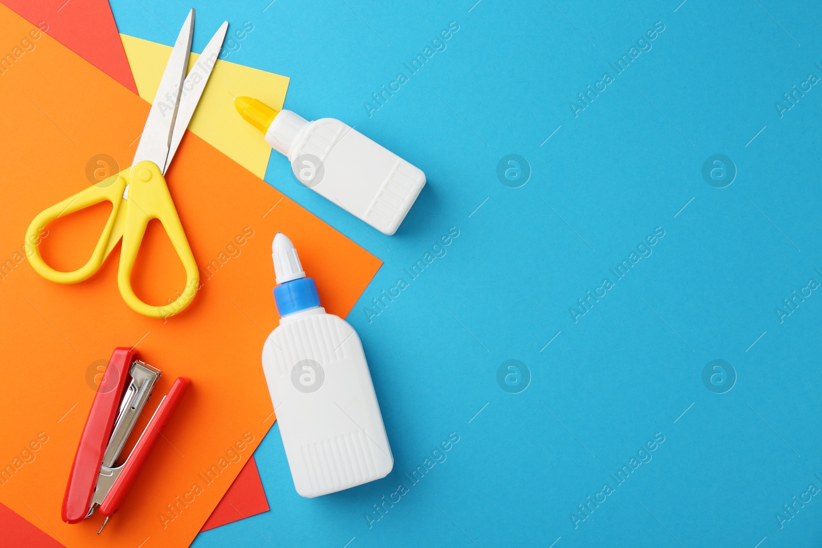 Photo of Glue, colorful paper, stapler and scissors on light blue background, flat lay. Space for text