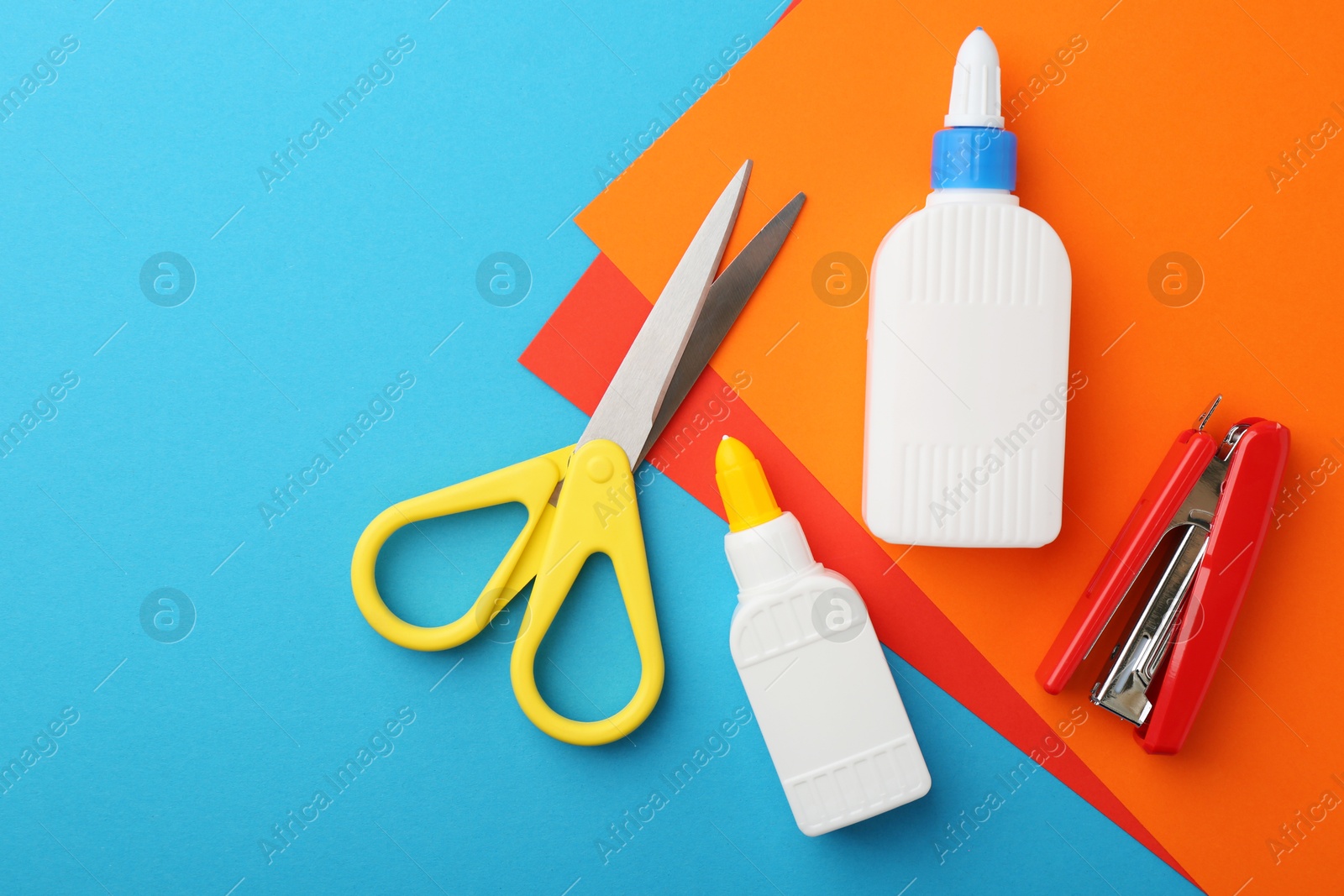 Photo of Glue, colorful paper, stapler and scissors on light blue background, flat lay. Space for text