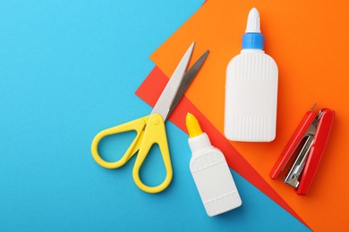 Photo of Glue, colorful paper, stapler and scissors on light blue background, flat lay. Space for text