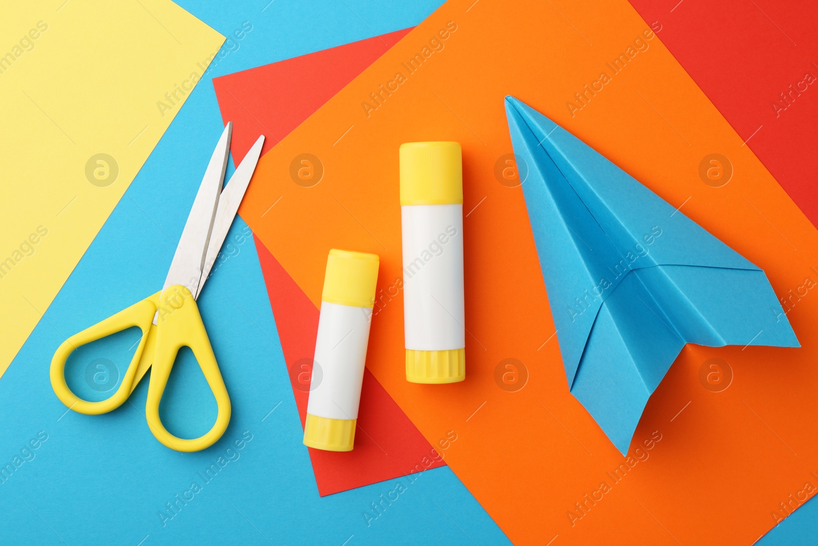 Photo of Glue, colorful paper and scissors on light blue background, flat lay